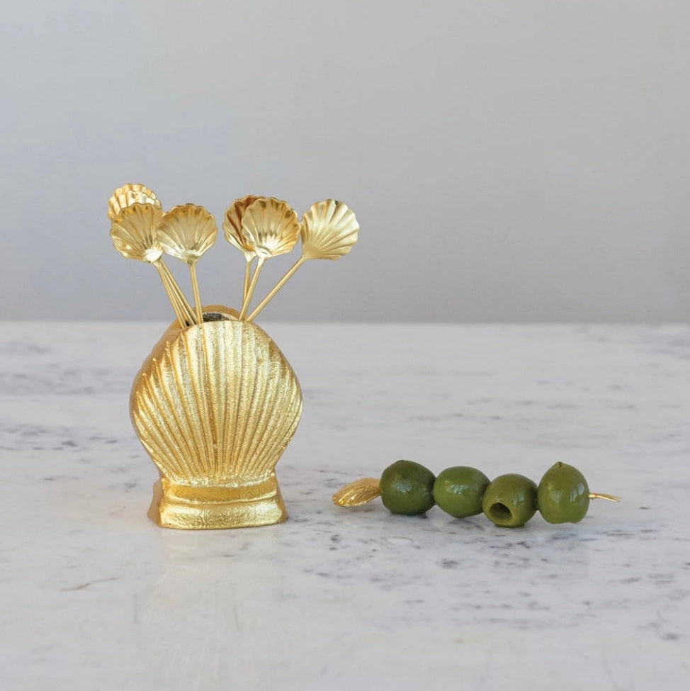 Gold shell-shaped olive holder with green olives on a marble surface