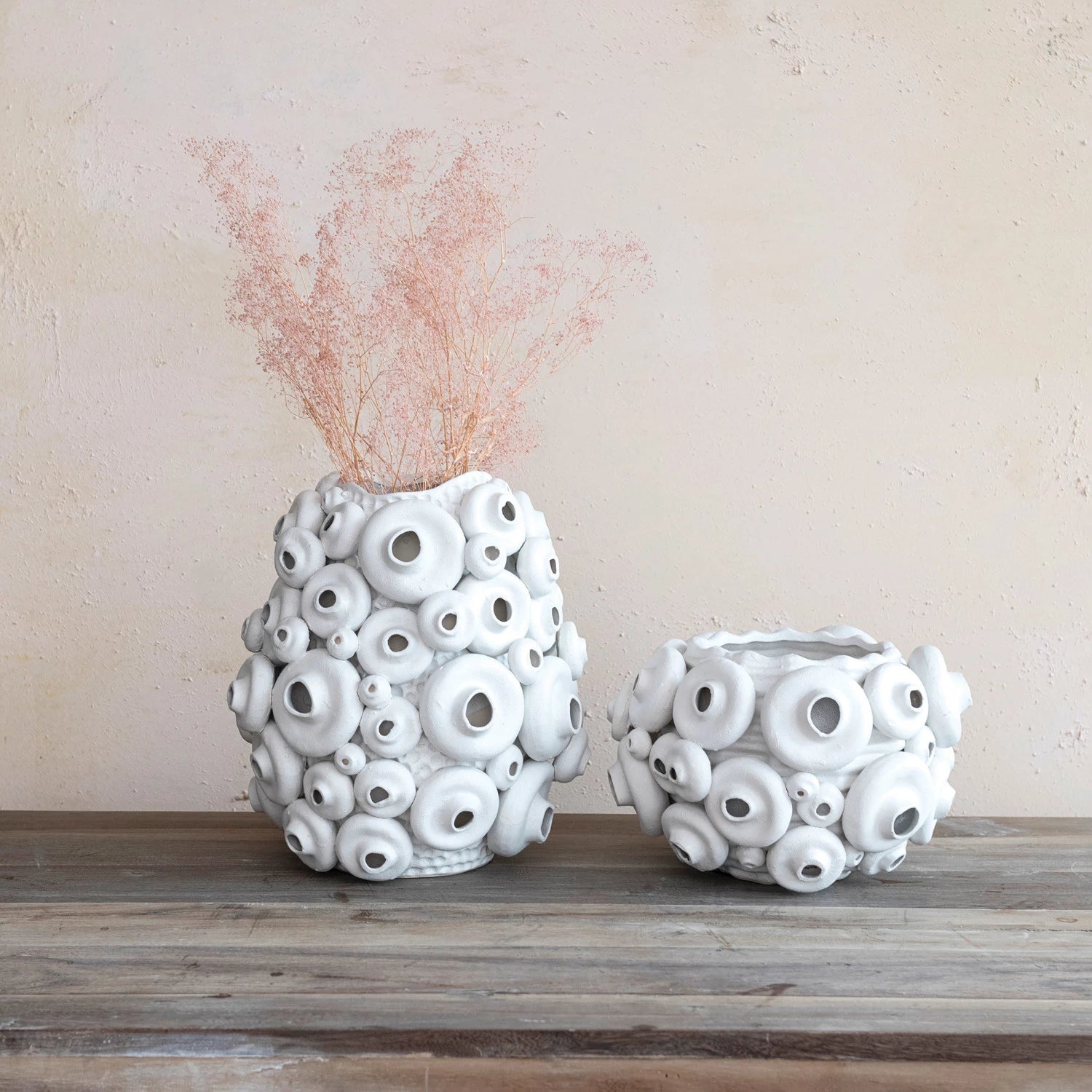 Two white textured vases on a wooden surface with a beige background