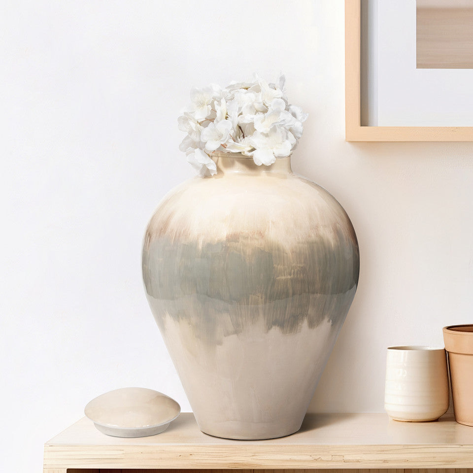 A white, iron Temple Vase with a floral arrangement on top, placed on a wooden surface in a home setting.