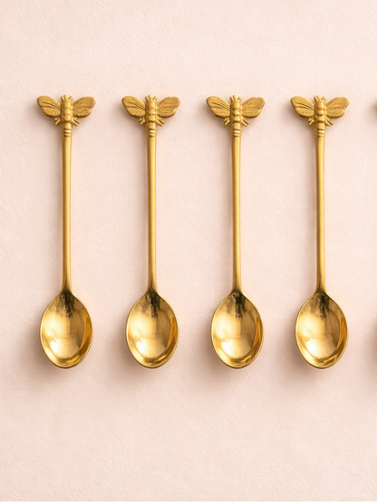 Four gold bee-shaped spoons on a pink background