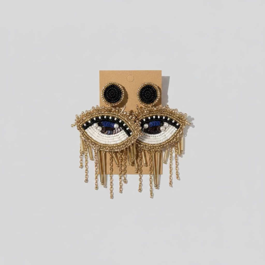 A pair of gold-colored earrings designed with eye embellishments, displayed against a neutral background.