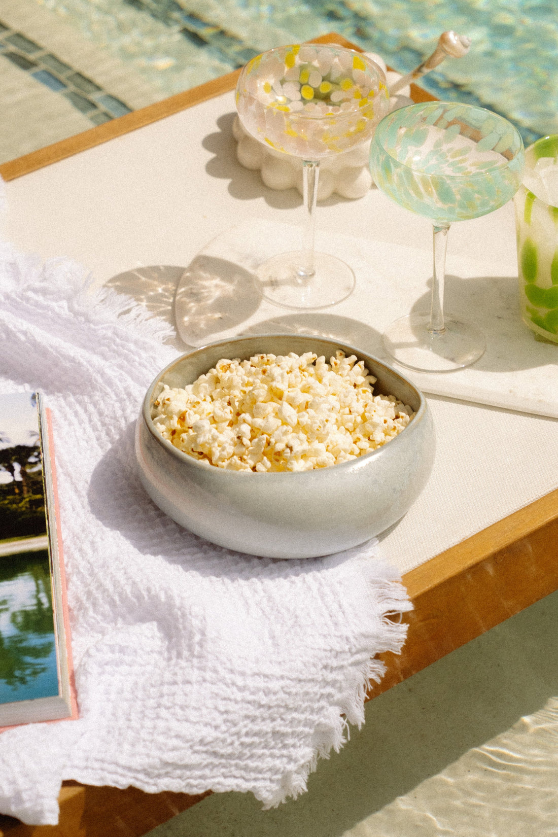 Bowl of popcorn and drinks on a table by a pool