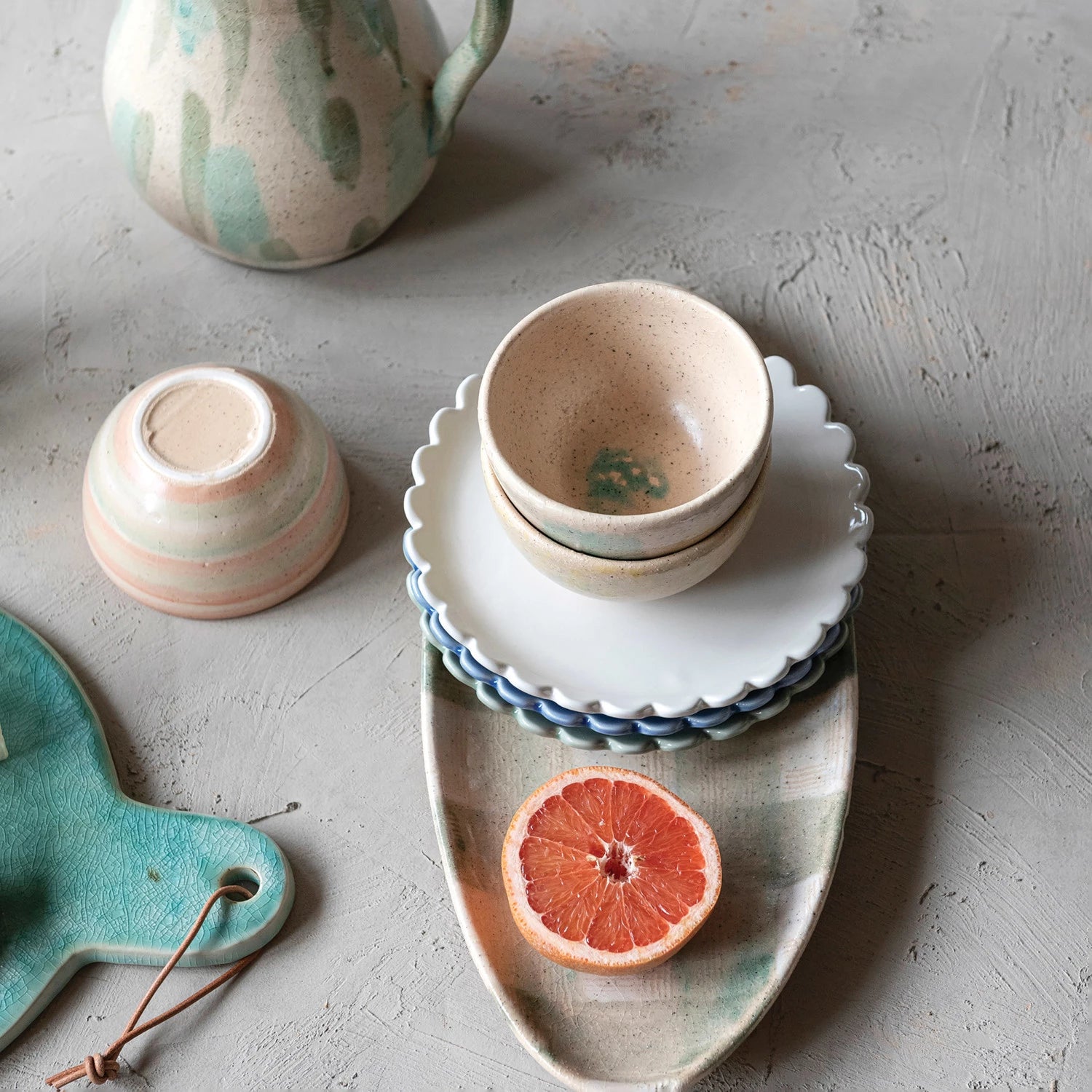 Ceramic bowls and a cutting board on a textured surface with a half-sliced grapefruit.